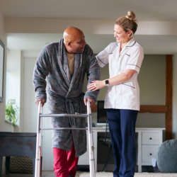 caregiver and elderly man walking inside the house