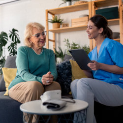 caregiver holding a tablet and talking to the elderly woman