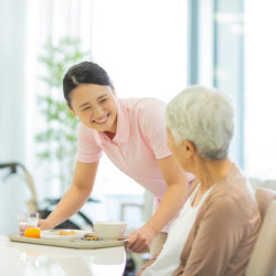 caregiver bringing food for the elderly woman