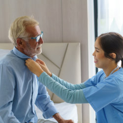 caregiver buttoning the elderly man's shirt