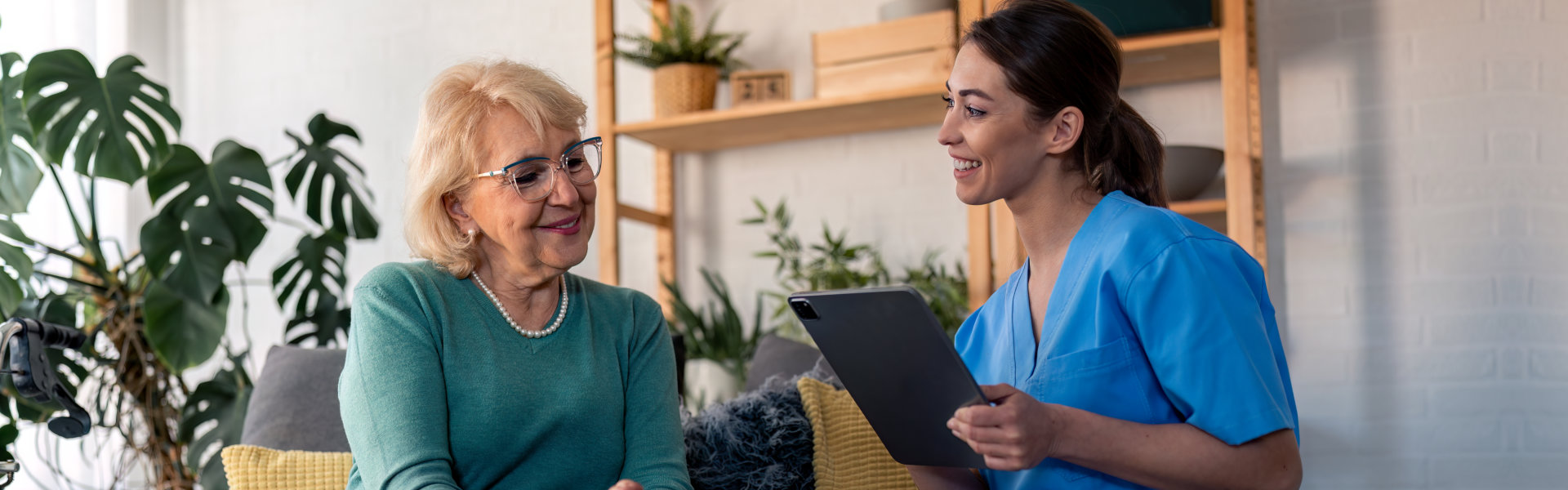 caregiver holding a tablet and talking to the elderly woman