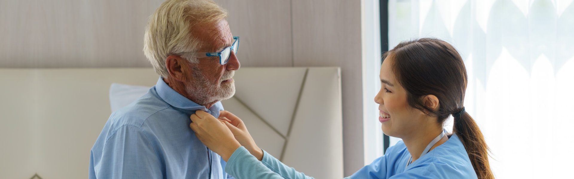 caregiver buttoning the elderly man's shirt